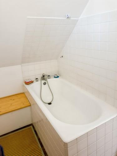 a white bath tub in a white tiled bathroom at La maison des Hortensias Vic-Sur-Cère, 10 pers in Vic-sur-Cère