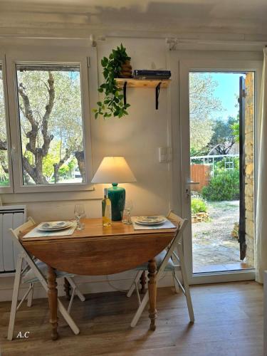 une table à manger avec une lampe et deux fenêtres dans l'établissement La Chambre Sous Les Oliviers - Très cocooning avec grand jardin, borne recharge électrique, à 5min du centre - BY AURAconciergerie, à La Cadière-dʼAzur