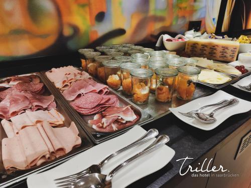 ein Buffet mit Speisen, Fleisch, Marmelade und Besteck in der Unterkunft Stay by Triller - Aparthotel in Saarbrücken
