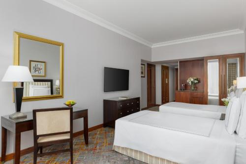 a bedroom with two beds and a desk and a mirror at Swissotel Al Maqam Makkah in Makkah