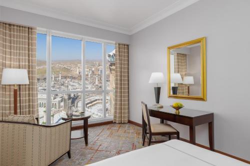 a hotel room with a desk and a large window at Swissotel Al Maqam Makkah in Makkah