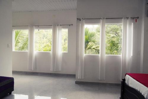 a bedroom with two windows with white curtains at Wilderstay Resort in Meppādi