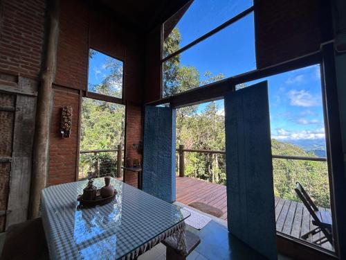 Una habitación con una mesa y grandes ventanales. en Refúgio na Mata - Casa de campo, en Santo Antônio do Pinhal