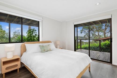 Habitación blanca con cama y ventanas grandes. en Whale Beach Abode, en Whale Beach