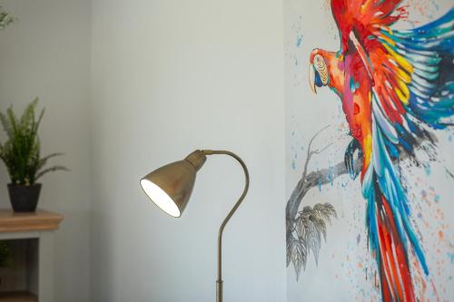 a painting of a parrot on a wall next to a lamp at Beautiful Barn Conversion - Orchard Escape for 12! in Cropthorne