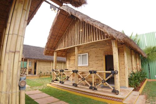 a house with a thatched roof with a wooden porch at Maharsh Bamboo Stays near Devanahalli in Dod Jāla