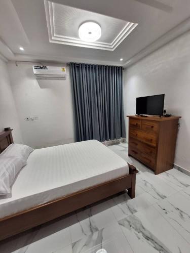 a bedroom with a bed and a television on a dresser at COD Haven Ventures Apartments in Madina