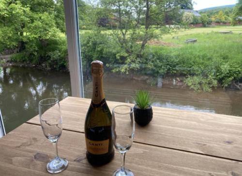 eine Flasche Wein mit zwei Gläsern auf einem Tisch in der Unterkunft Riverbank Cottage River Ehan Double Balcony in Egremont