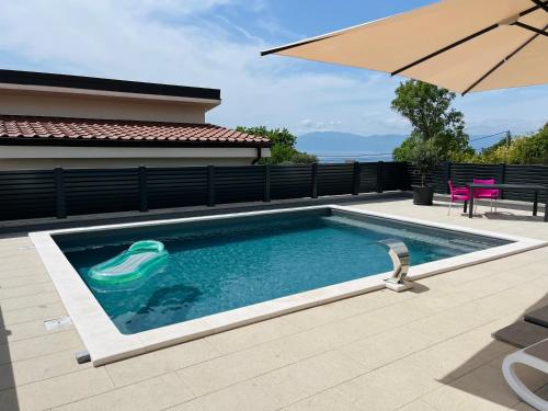 a swimming pool with an umbrella next to a house at Apartman Dora in Šmrika