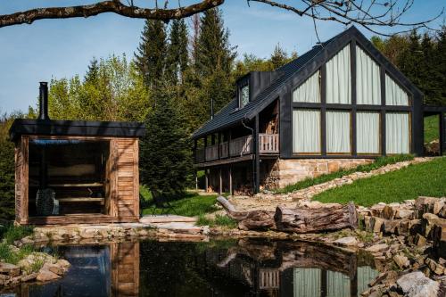una casa con techo negro y un reflejo en el agua en Chata Pytlorka Beskydy offgrid wellness, en Zahŭří