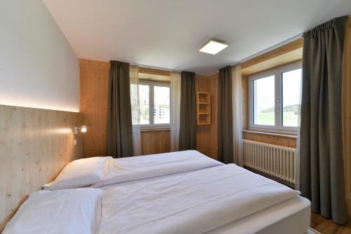 a bedroom with a large white bed and two windows at Hotel Maloja Kulm in Maloja