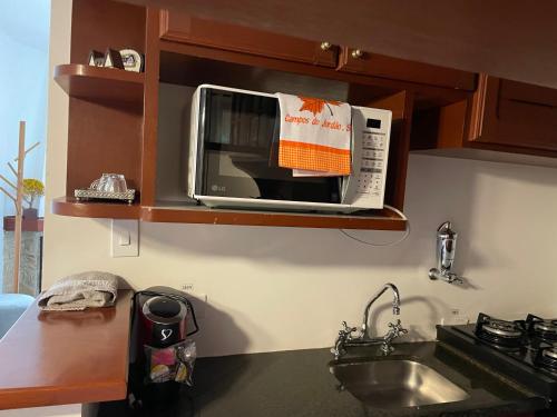 a microwave on a shelf above a sink in a kitchen at Quatre Saisons Residence in Campos do Jordão