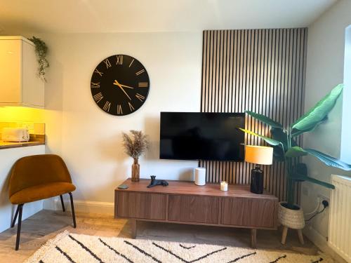 a living room with a tv and a clock on the wall at Stylish apartment 1 min to town centre and harbour in Lymington