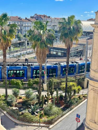 a blue train traveling through a city with palm trees at Hôtel Colisée-Verdun Centre Gare Saint-Roch in Montpellier
