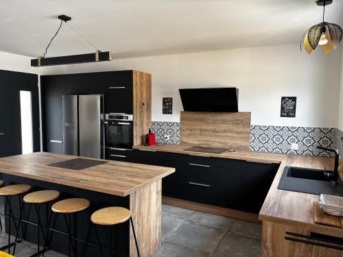 une cuisine avec des placards noirs et un îlot de cuisine avec des tabourets dans l'établissement Gîte de Montfort, à Caromb