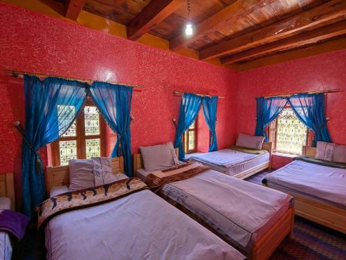 a room with four beds and windows with blue curtains at Gite D'etape Ait Ali Nito Assounfou in Megdaz