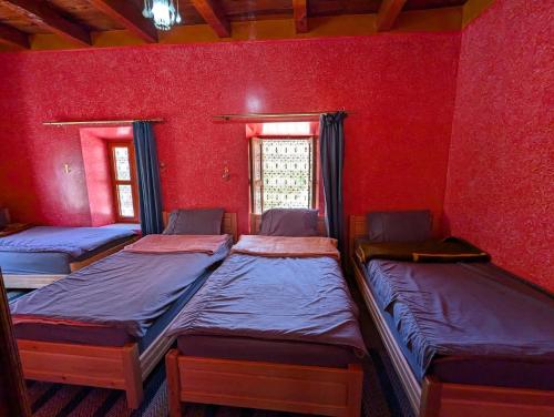three beds in a room with a red wall at Gite D'etape Ait Ali Nito Assounfou in Megdaz