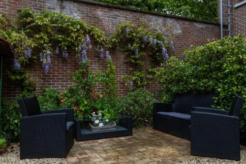 a garden with two chairs and purple flowers on a brick wall at Hotel De Pastorij in Leuven