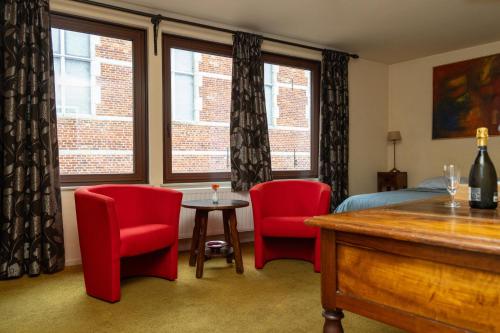a bedroom with two red chairs and a bed and windows at Hotel De Pastorij in Leuven
