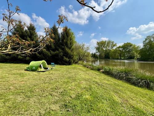une tente posée sur l'herbe au bord d'une rivière dans l'établissement Rives du Bel Air - Hébergement & caravaning -, à Passais-la-Conception