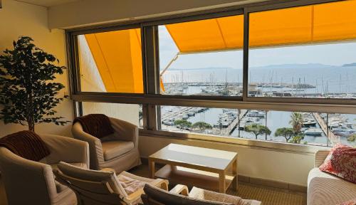 une salle d'attente avec des chaises, une table et une grande fenêtre dans l'établissement Très bel appartement T3 dernier étage vue mer, au Lavandou
