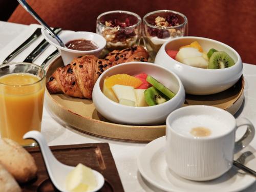 a tray of food with bowls of fruit and a drink at Mövenpick Grand Hotel Wroclaw in Wrocław