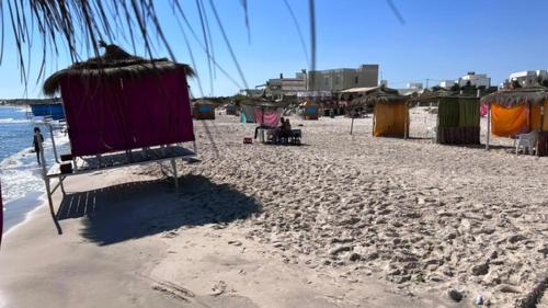 a sandy beach with a hut and the ocean at Résidence Le Marin in Banī ‘Aţāʼ
