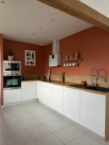 - une cuisine avec des placards blancs et des murs orange dans l'établissement Villa l'Esneval & Spa - Normandie, à proximité d'Etretat, à Criquetot-lʼEsneval