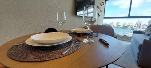 a wooden table with two glasses and plates and a bowl at Parque do Cais - Flats Premium no Recife por Yolo in Recife