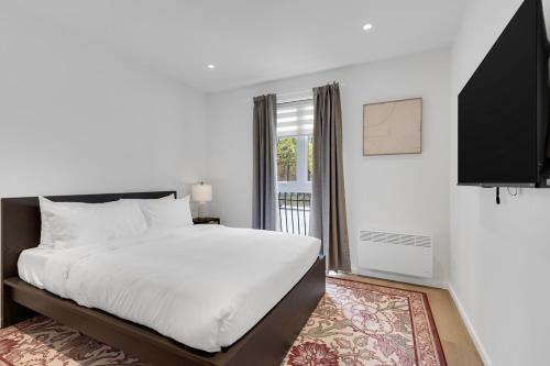 a white bedroom with a bed and a window at Le Victoria Midtown Mtl in Montréal