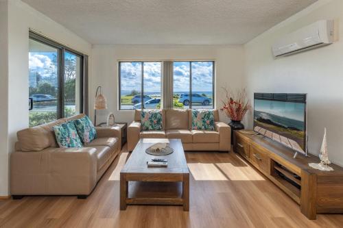 a living room with a couch and a flat screen tv at Sandpebbles 1 Pebbly Beach in Forster
