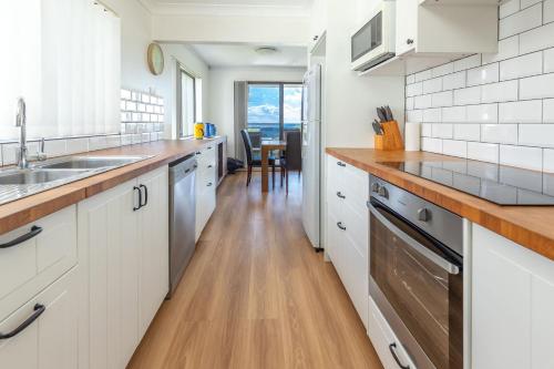 a kitchen with white cabinets and a wooden floor at Sandpebbles 1 Pebbly Beach in Forster