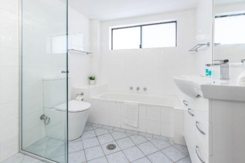 a white bathroom with a tub and a toilet and a sink at Sandpebbles 1 Pebbly Beach in Forster