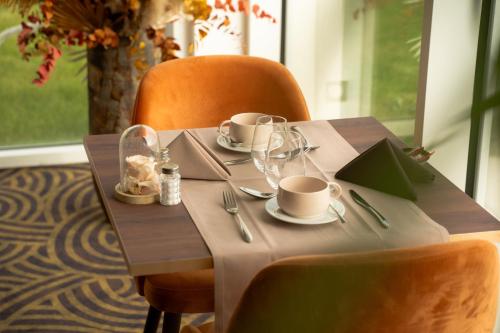 a wooden table with cups and saucers on it at Hôtel Le Manoir du Roselier in Plérin