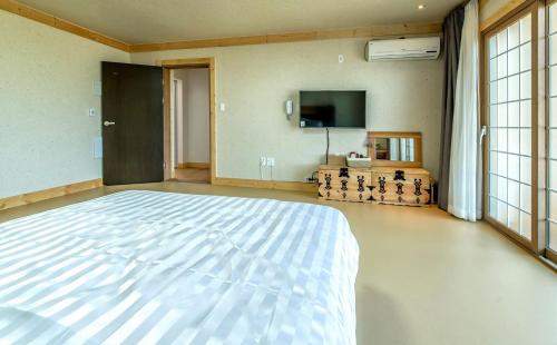 a large bedroom with a white bed and a flat screen tv at Bada Maru Pension in Seogwipo