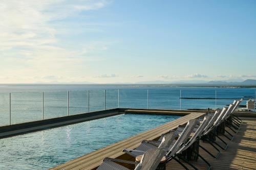 a swimming pool on a deck with chairs and the ocean at Iberostar Selection Es Trenc -New Opening- in Colonia Sant Jordi