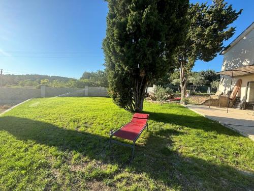 a red bench sitting in the grass near a tree at Brin d'Olivier en Luberon in Gargas
