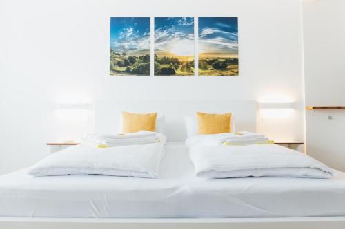 two beds in a white bedroom with two paintings on the wall at Rosenalm Scheidegg in Scheidegg