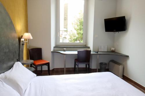 a bedroom with a bed and a desk and a window at Hôtel Le Lons in Foix
