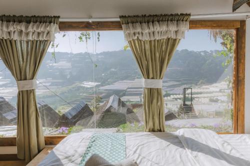 ダラットにあるMái Lá Homestay & Herbal Spaのベッドと大きな窓のある寝室