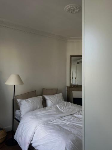 une chambre avec un lit avec des draps blancs et une lampe dans l'établissement Bel appartement Haussmanien, à Paris