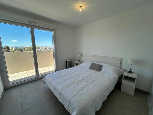 une chambre blanche avec un lit et une grande fenêtre dans l'établissement NAÏA ALO, à Sérignan