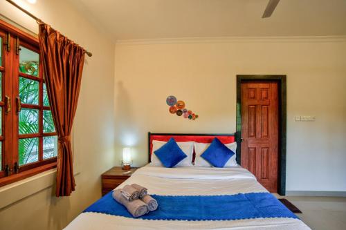 a bedroom with a bed with blue pillows and a window at Coastal Bliss By Masaka in Anjuna