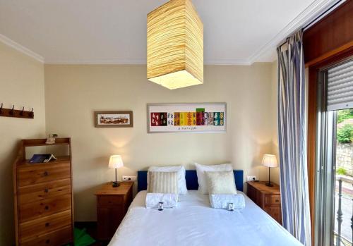 Un dormitorio con una cama blanca y una lámpara de araña. en Holibai, Chuliña, Cerca de la playa, con piscina y parking, en Baiona