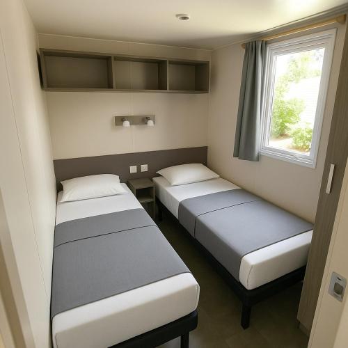 deux lits dans une petite pièce avec une fenêtre dans l'établissement Mobil Home XL 6 places - Camping Les Sablines - Bord de mer, à Vendres