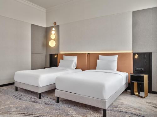two beds in a hotel room with white sheets at Mövenpick Grand Hotel Wroclaw in Wrocław