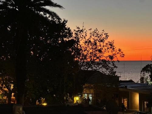 a sunset over the water with a tree and a building at Casa Lahusen in Colonia del Sacramento