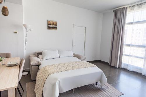 a white bedroom with a bed and a desk at Maya Bay Suites in Alicante