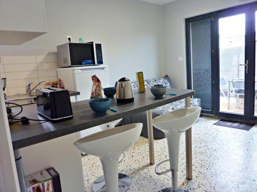 une cuisine avec un comptoir et deux tabourets blancs dans l'établissement Appartement T2 rénové, climatisé, avec terrasse et parking, proche plage - FR-1-387-166, à Marseillan