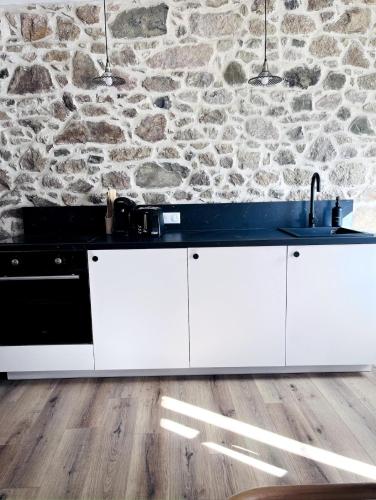 - une cuisine avec des placards blancs et un mur en pierre dans l'établissement Petite maison de charme, à Châtelaudren-Plouagat